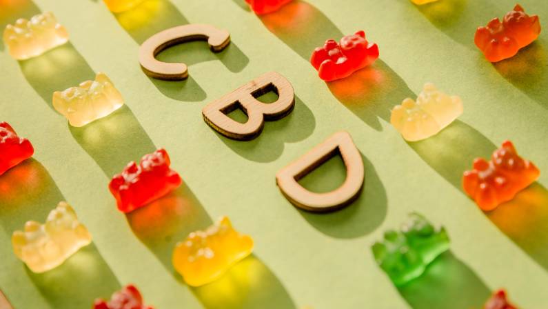 Photo of Wooden letters CBD on a green background and gelatin in the form of bears.