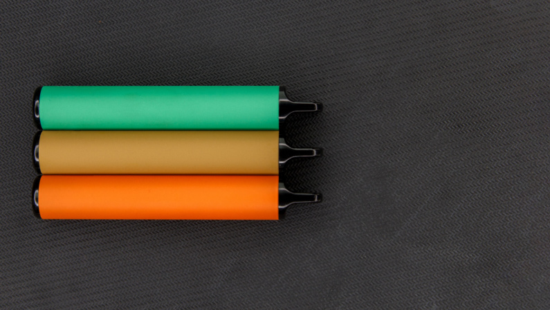 Disposable e-cigarettes on dark background top view, mocap. green orange