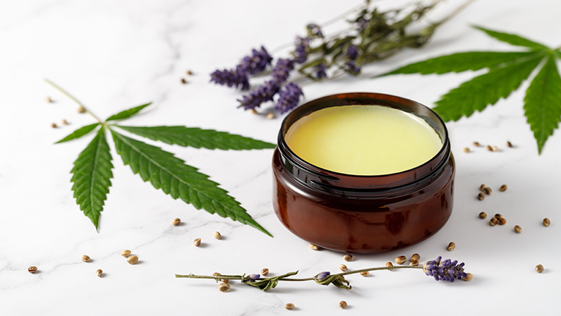 Composition with cannabis wax salve or cream with lavender extract, flowers, hemp leaves and seeds on marble background with copy space. Cannabis products