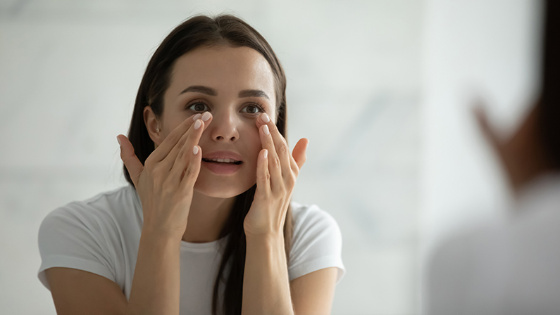 Close up smiling young woman applying moisturizing cream on under eye