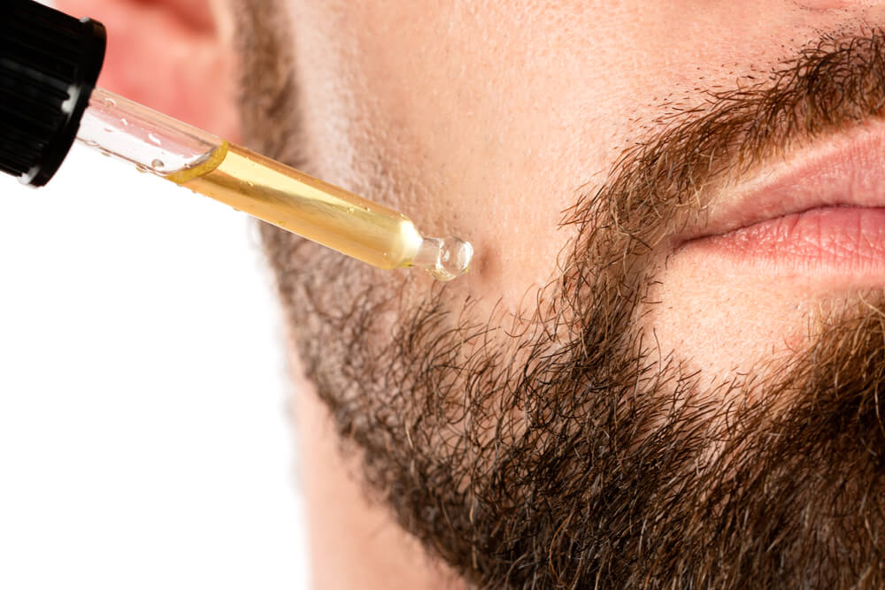 Closeup of male face and pipette with a cbd oil for a beard growth and moisturize skin 