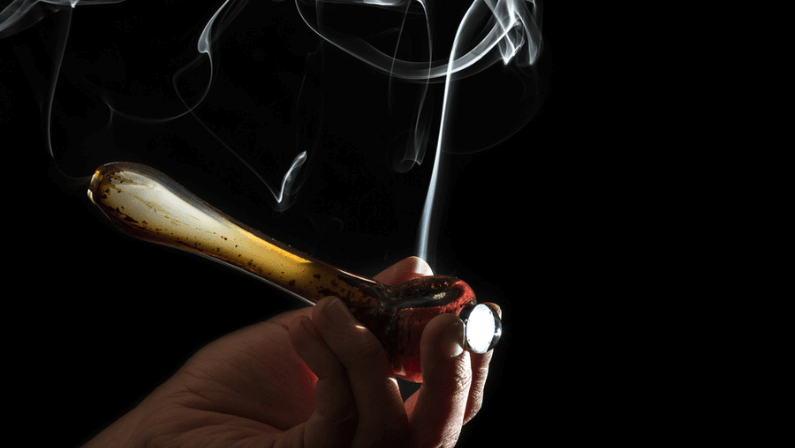 High contrast studio shoot of a pipe with simulated marijuana smoke on a dark background