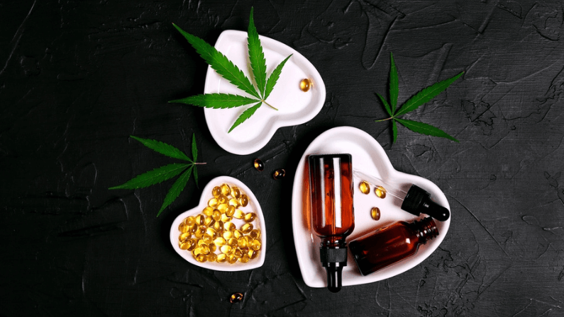 Heart saucers with glass bottles with cbd oil, capsules and hemp leaves on black background. Top view, flat lay. Alternative medicine. Essential natural oils for cosmetics.